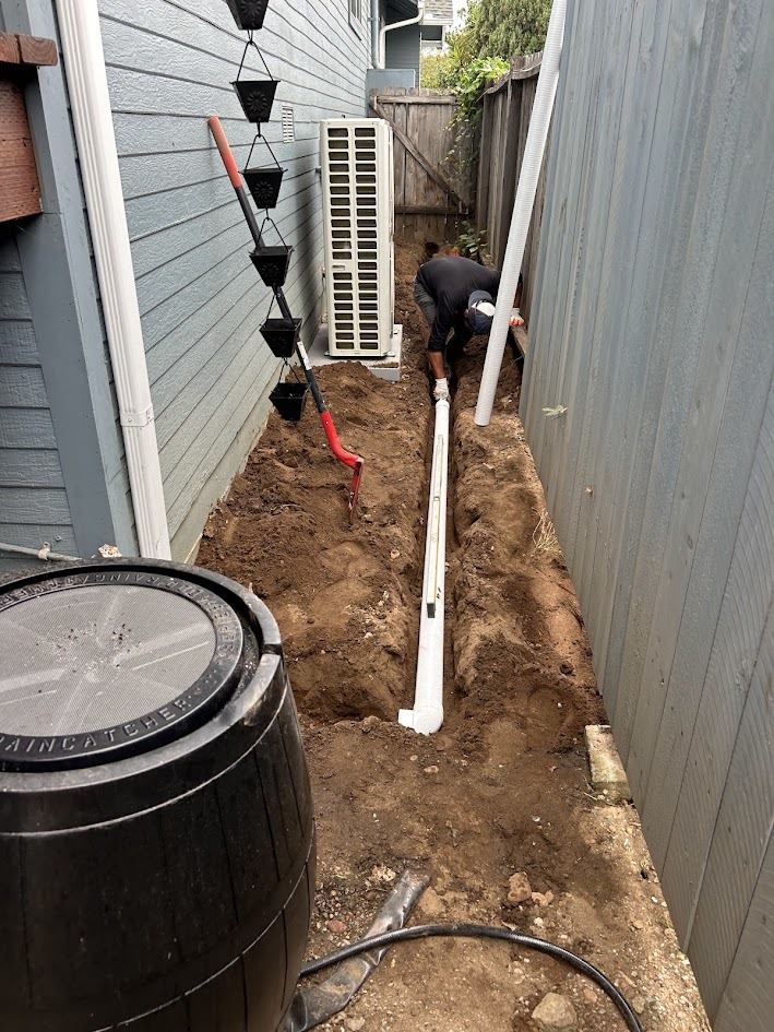 French drain trench installation along a side yard, connecting a downspout drain line