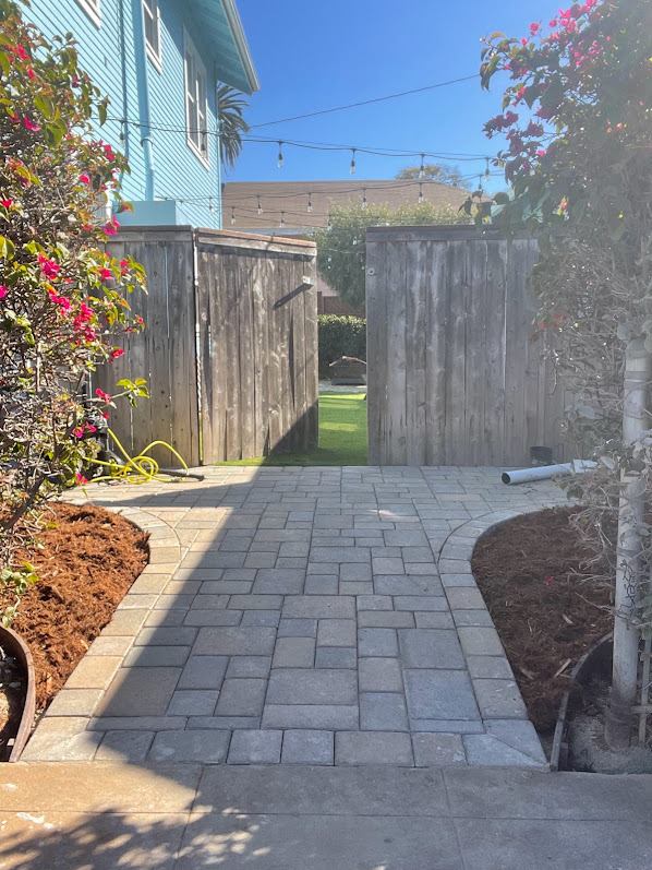 Curved paver walkway leading to a side gate, bordered by planting beds in San Diego