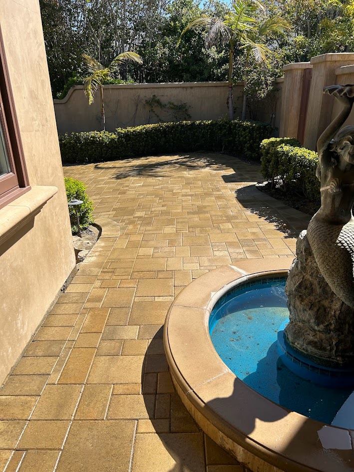 Side courtyard paver installation bordered by hedges and a stucco wall